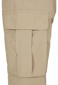 Beige kravas bikses ar priekšējo kabatu, ar plisēm un redzamām stitchingu detaļām. Izgatavotas no viegla auduma, ar teksturētu virsmu.