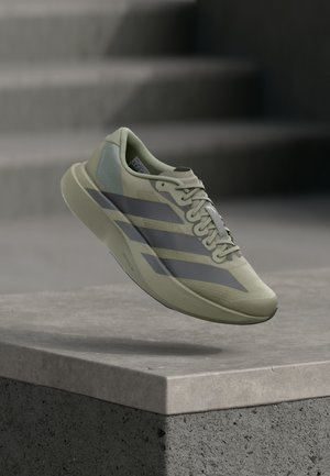 Light green running shoe with dark stripes suspended above a concrete ledge, with stone steps in the blurred background.