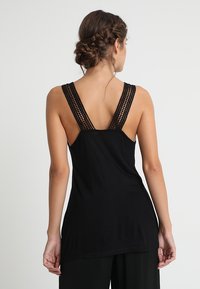 Black tank top with wide, textured lace straps, featuring a relaxed fit and a smooth fabric finish. Back view shows lace detail.