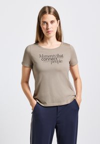 Camiseta de manga corta en color verde oliva con un cuello redondo y texto en negro: "Momentos que conectan a las personas." Tejido suave y liso.