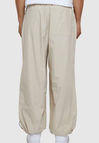 Lys beige, løstsiddende bukser med elastisk talje og snor. Har en enkelt baglomme og elastiske manchetter ved anklerne.