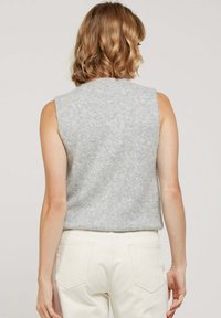 Top sans manches gris en tissu doux et texturé. Présente un col arrondi et une coupe décontractée, associé à un jean de couleur claire.