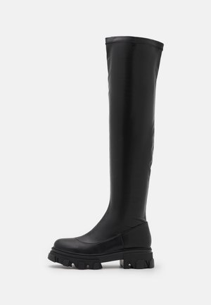 Czarne, wegańskie botki do kolan z grubą podeszwą, gładką teksturą, zaokrąglonym noskiem i minimalnymi detalami szwów na białym tle.