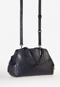 Borsa a tracolla in pelle blu scuro con forma strutturata, doppi manici e spallaccio regolabile. Caratterizzata da una superficie liscia e chiusura con zip.