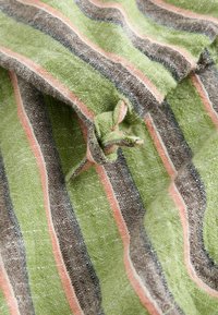 Tissu vert à rayures roses, marron et grises avec un petit nœud noué au centre sur un matériau en lin texturé.