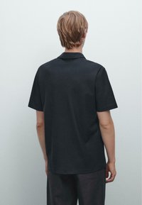 Polo shirt nero a maniche corte con colletto, caratterizzato da una texture liscia e un design minimalista. Senza loghi o motivi visibili.