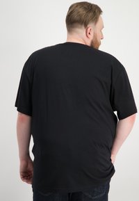 T-shirt nera a maniche corte con vestibilità rilassata, realizzata in materiale morbido, con collo rotondo e texture liscia. Vista posteriore visibile.