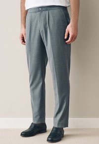 Graue, maßgeschneiderte Hose mit dezentem Karomuster, ausgestattet mit flacher Vorderseite, leicht zulaufenden Beinen und Knopfverschluss in der Taille.