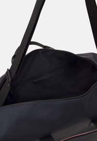 Laatikko sininen kangaskassi, jossa on sileä pinta, avara musta sisustus, päällinen vetoketju ja pieni sisätasku.