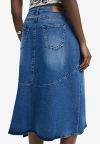 Der Denim-Midirock zeichnet sich durch ein ausgestelltes Design, einen rohen Saum und kontrastierende Nähte aus. Die Rückentaschen und das Markentag am Bund verleihen zusätzliche Details.