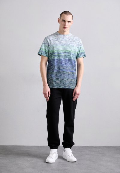 Herre kortermet t-skjorte i grønn og blå gradient med horisontale striper; kombinert med svarte joggebukser og hvite sneakers.