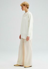 Witte gebreide trui met een textuurkragen, gecombineerd met crèmekleurige wijde broek en gouden loafers. Eenvoudig ontwerp en lichte kleuren.