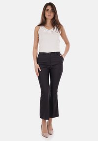 Pantaloni neri a zampa d'elefante con vestibilità sartoriale, vita alta e tasche frontali, abbinati a un top bianco senza maniche con dettagli floreali.