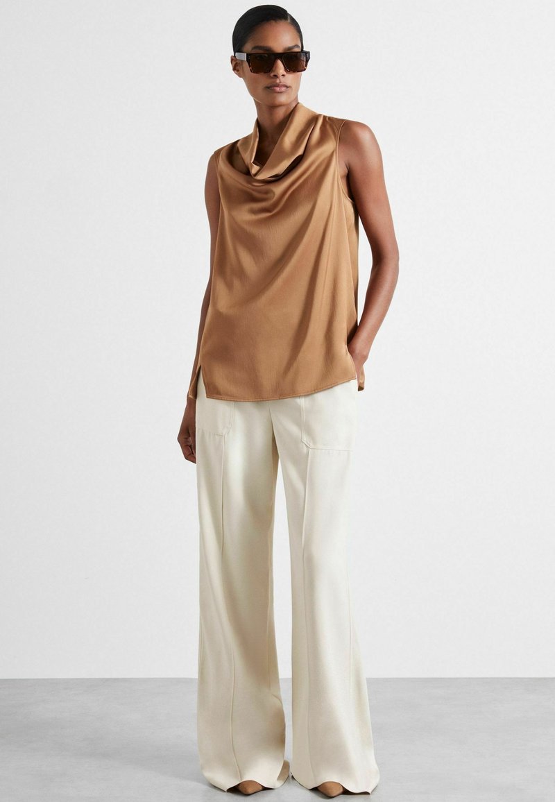 Brown cowl-neck sleeveless top paired with cream wide-leg trousers. Both garments feature a smooth texture and modern design.