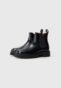 Bottes Chelsea en cuir noir avec des panneaux latéraux élastiques, des pointes arrondies et des languettes de tirage. Caractérisées par une semelle en caoutchouc robuste pour une meilleure adhérence.