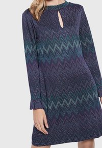 Abito a maniche lunghe di colore viola con un motivo a zig-zag in teal e blu. Presenta un colletto a chiave e polsini a balze.