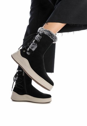 Stivaletti alla caviglia in suede nero con colletto in pelliccia sintetica, suola bianca e dettaglio con lacci. Presentano una zip laterale per una facile vestibilità.