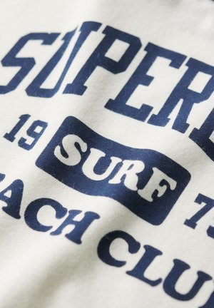 Weißer Stoff mit navyblauen Textdesign, das "SUPER" und "SURF BEACH CLUB" in fetter Schrift zeigt. Glatte Textur mit einem lässigen Stil.