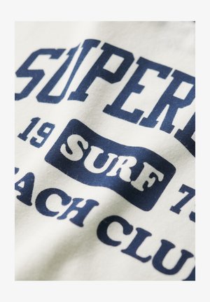 Witte stof met marineblauwe tekstontwerp featuring "SUPER" en "SURF BEACH CLUB" in vette letters. Gladde textuur met een casual stijl.