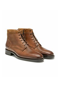 Bottes en cuir marron à tige courte avec une finition lisse, présentant un bout arrondi, un système de laçage à l'avant et une fermeture éclair sur le côté. Le col en daim texturé couleur tan accentue l'ensemble.