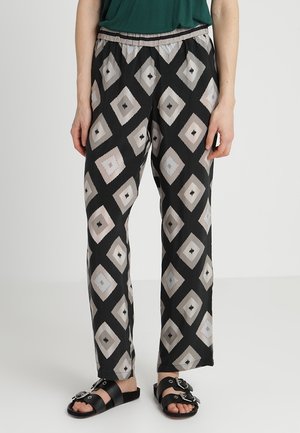 Czarne spodnie z beżowo-szarymi wzorami diamentowymi, noszone z zielonym topem i czarnymi sandałami na klamrę, widoczne od talii do stóp.