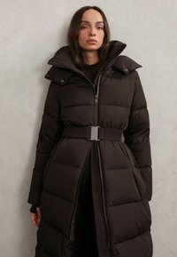 Giacca imbottita marrone con vita cinturata, collo alto e apertura frontale con zip. Presenta una texture trapuntata e tasche laterali.