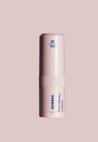 Un tubo de lápiz labial rosa claro con una sección media texturizada. Texto azul que muestra "KORRES True Velvety Lipstick" y valores numéricos en la tapa.