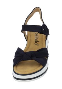 Sandal de cuña de tela en color navy con una tira delantera anudada, hebilla ajustable en el tobillo, plantilla acolchada en color marrón y suela en blanco y negro.