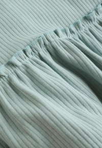 Tissu bleu clair à côtes avec des détails froncés le long du bord supérieur. Texture douce avec des lignes horizontales et un léger éclat.