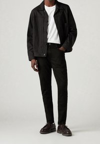 Chaqueta ligera negra, camiseta blanca, jeans ajustados negros y zapatos marrón oscuro. Detalles notables incluyen botones y una sutil textura en la tela.