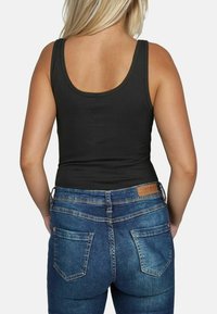 Zwarte tanktop met dunne spaghetti-bandjes, gecombineerd met blauwe denim jeans. De jeans hebben twee achterzakken en een leren merklabel op de tailleband.