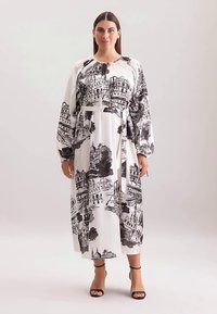 Maxikleid aus weißem Stoff mit schwarzem architektonischem Muster. Mit langen Ärmeln und einem Taillengürtel. Glatte Textur und entspannte Silhouette.