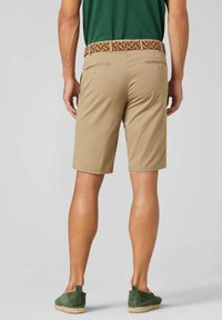 Beige shorts met een rechte pasvorm, voorzien van twee achterzakken en een kleurrijke geweven riem. G gedragen met groene instappers op blote benen.