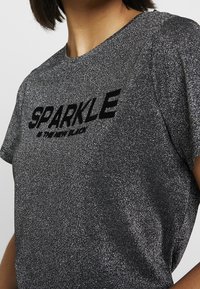 Černé metalické tričko s krátkým rukávem, které má na přední straně vystouplý černý nápis "SPARKLE" s třpytivým, texturovaným povrchem.