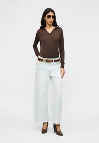 Καφέ πόλο πουκάμισο με μακριά μανίκια, ανοιχτό μπλε τζιν παντελόνι με φαρδιά πόδια και σκούρα καφέ παπούτσια με τακούνι. Συνδυασμένο με χρυσή ζώνη και γυαλιά ηλίου.