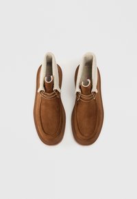 Brune ruskind ankelstøvler med en cremet fleeceforing, der har en rund tå, snøre-design og gummisåler med struktureret greb.