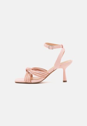 Rausvos kulninės šlepetės su mazgo dizainu, plonomis juostelėmis ir kulkšnies sagtimi. Ypatumas - glotnus, blizgus paviršius ir smailas pirštas.