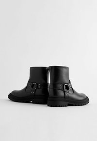 Schwarze Leder-Stiefeletten mit einem seitlichen Schnallenverschluss, texturiertem Gummisohle und verstärkter Zehenkappe. Sie verfügen über eine glatte Oberfläche und eine robuste Konstruktion.