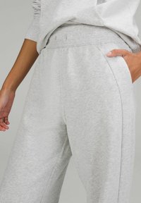Hellgraue Sweatpants mit weicher Textur, elastischem Bund, Seitentaschen und lockerer Passform, die feine Steppdetails aufweisen.