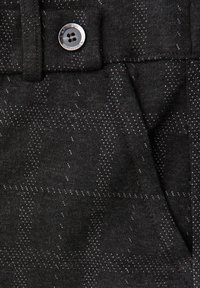 Tmavě šedá látka s jemným diamantovým vzorem, se stříbrným knoflíkem a kontrastním šitím. Hladká textura a přizpůsobený design.