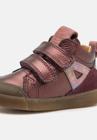 Chaussure en cuir bordeaux avec trois bandes Velcro, tige texturée et accents irisés. Caractéristiques d'une semelle en caoutchouc et d'un talon prononcé.