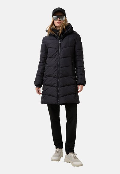 Black puffer coat with quilted design, hood, and full zipper, paired with black pants and light-colored sneakers. Includes reflective sunglasses.