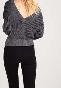 Texturerad, rutig grå tröja med V-halsdesign, tillsammans med svarta åtsittande byxor. Outfiten har en avslappnad passform och elastiska tyger.