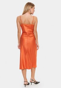 Satin oranje midi-jurk met dunne bandjes en een zijsplit, met een gladde textuur en een aansluitend ontwerp. Draag met zwarte hakken.