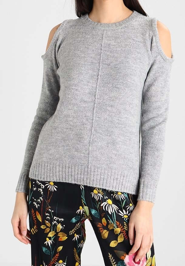 Grauer Strickpullover mit kalten Schultern und geripptem Saum. Gemusterte Blumenhose mit lebendigen Farben und verschiedenen Blumenformen.
