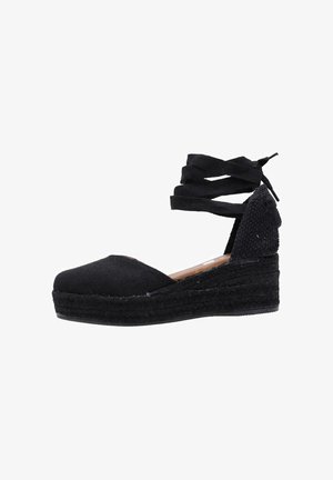 Wedge espadrille noire avec une tige en toile, semelle en jute tressé et sangles de cheville croisées. Bout rond et talon texturé.