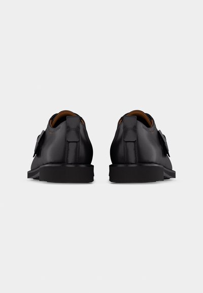 Paire de chaussures habillées en cuir noir avec détail boucle, vues de dos sur un fond gris clair uni.