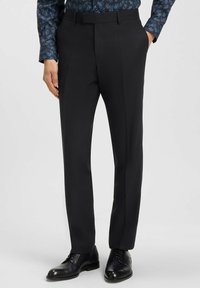 Pantaloni tailored neri con una texture liscia, dotati di pieghe frontali e design a gamba dritta, abbinati a scarpe nere lucidate.