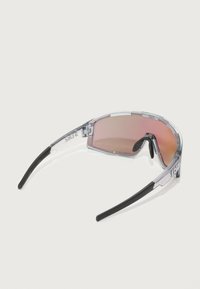 Óculos de sol com armação transparente e lentes cor-de-rosa, design curvado, pontas das hastes pretas e logótipo na lateral. Leves e com uma estética desportiva.