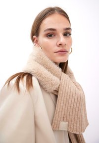 Beige ribbet strik scarf med en luksuriøs fake fur krave, prydet med et logo. Materialet fremstår blødt og struktureret, velegnet til koldere vejr.